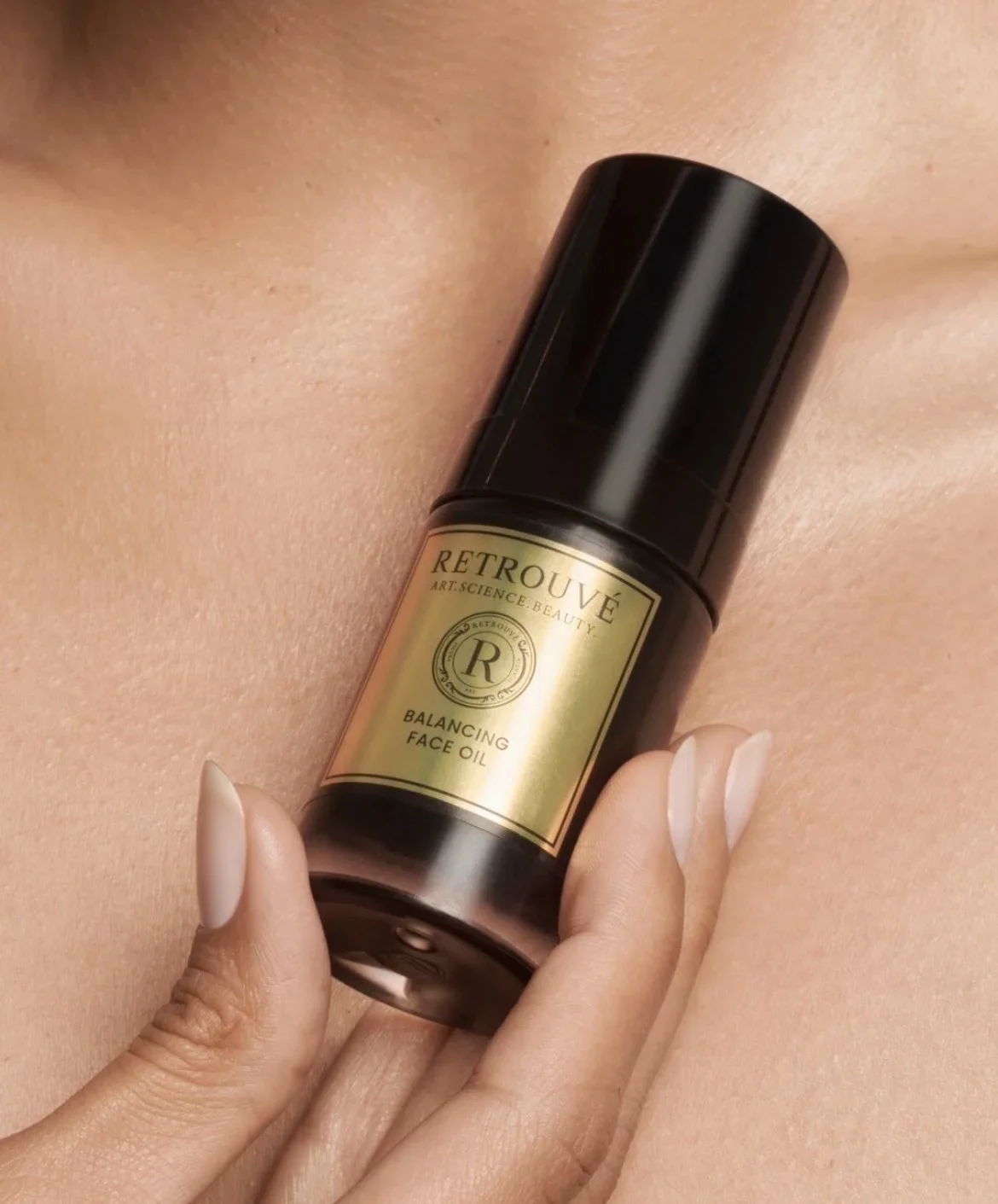 A bottle of Retrouvé Balancing Face Oil held against a woman's bare shoulder.