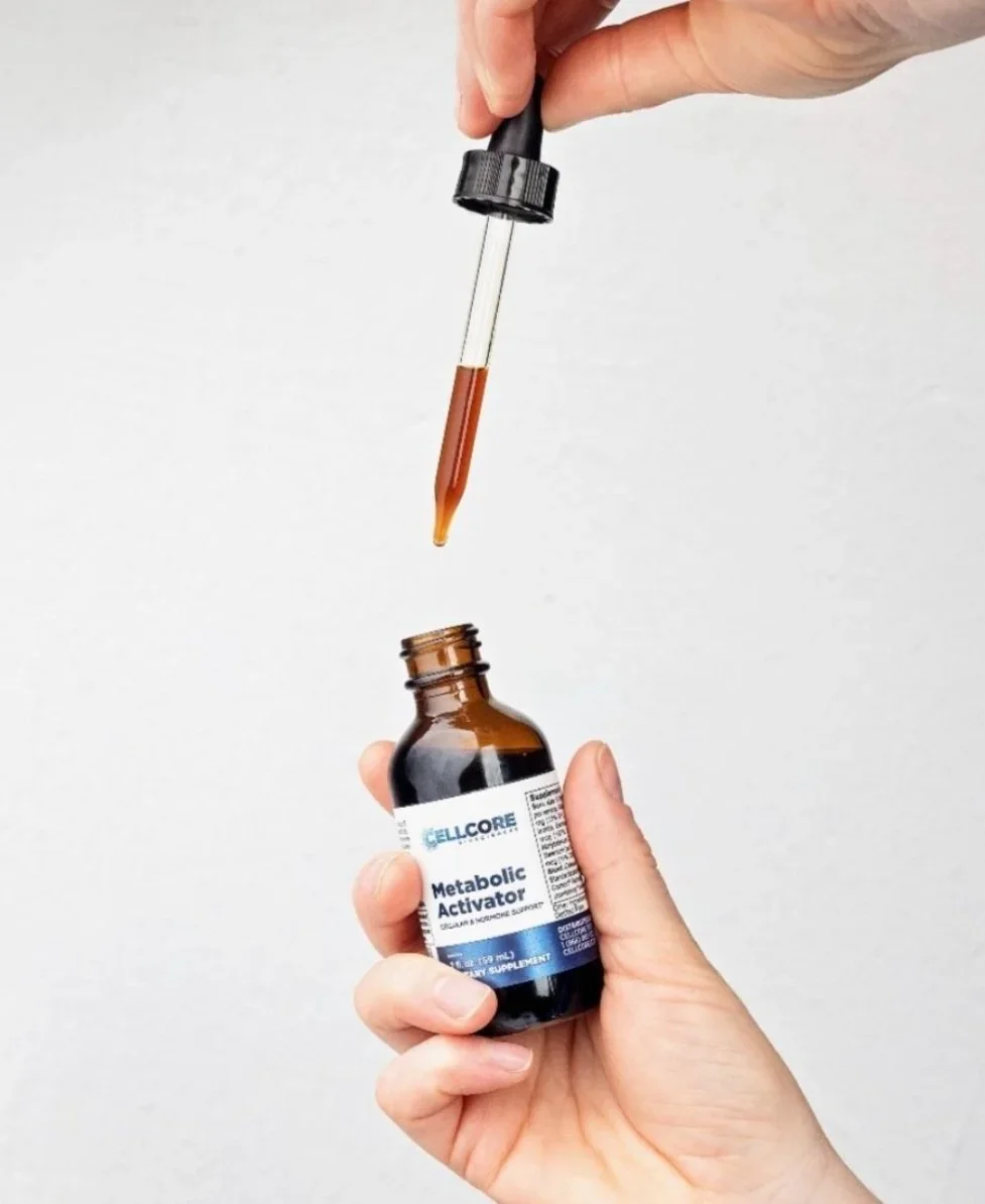 A person holding a brown glass bottle labeled 'Metabolic Activator' and a dropper releasing a brown liquid into the bottle.