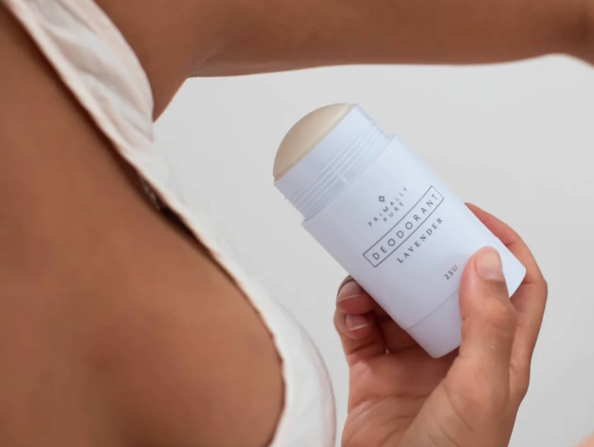 A person holding a white container of lavender-scented deodorant near their underarm, preparing to apply it.