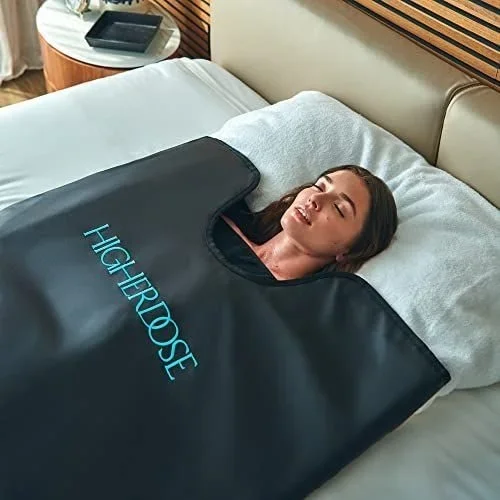 A woman lying on a bed covered by a black HYPERROBE blanket, resting her head on a pillow in a bedroom.