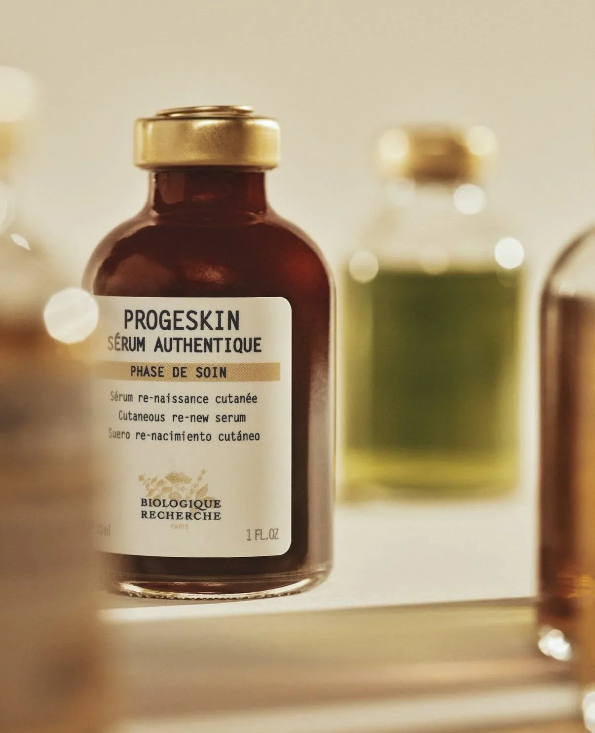A brown bottle labeled 'Progeskin Serum Authentique' with gold cap, surrounded by other skincare bottles on a shelf.