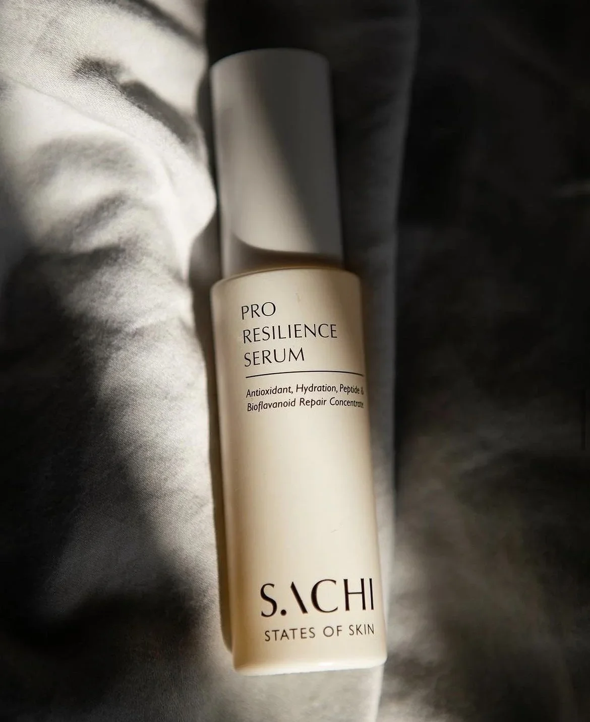 A bottle of SACHI Pro Resilience Serum resting on fabric with soft lighting.