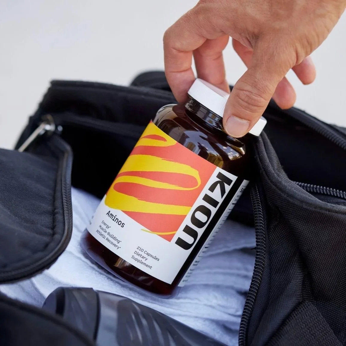 Person reaching into a black bag to take out a bottle of amino supplement labeled 'Kion' with yellow and red branding.
