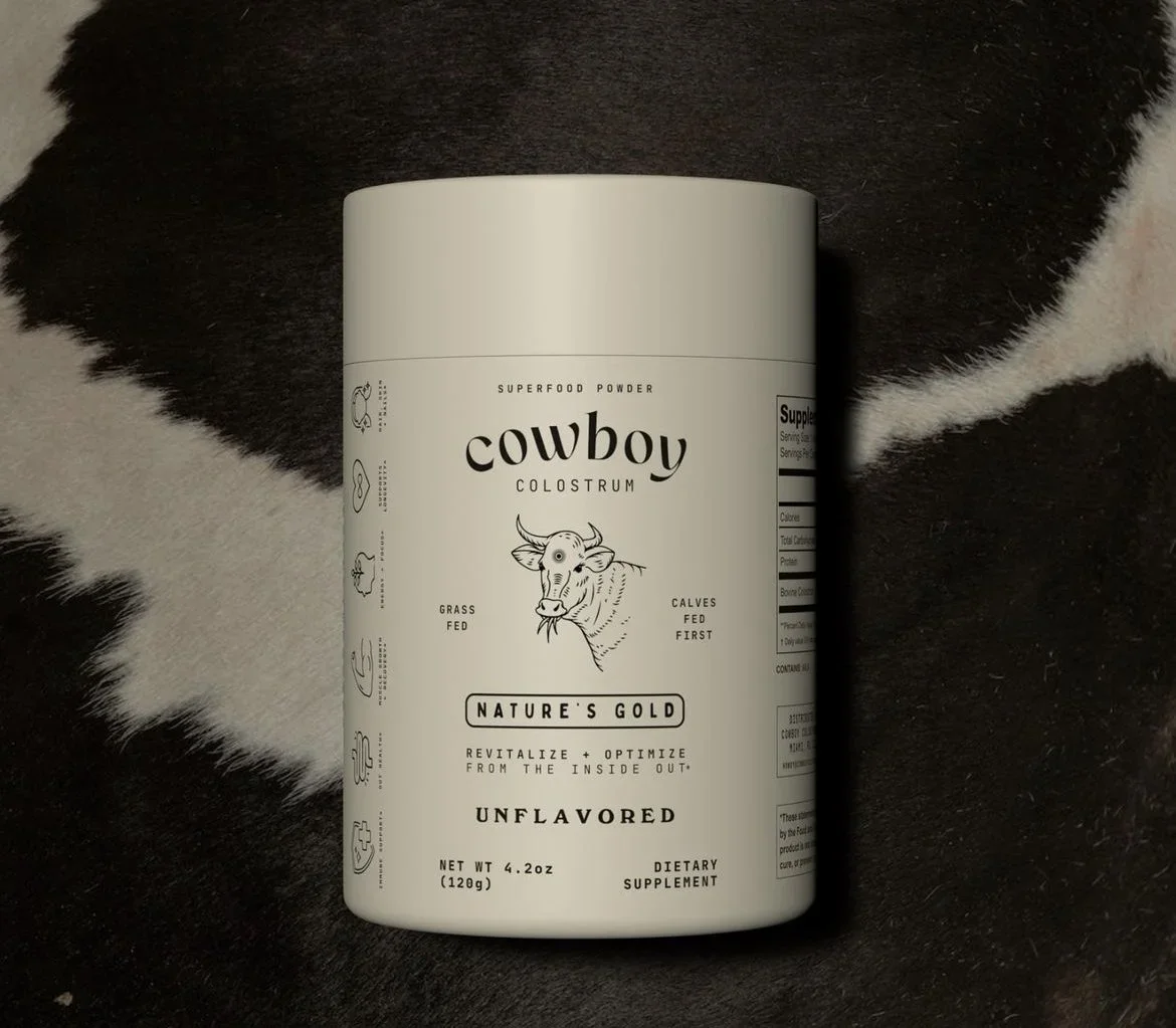 A white container of Cowboy Colostrum superfood powder on a black and white cowhide rug.