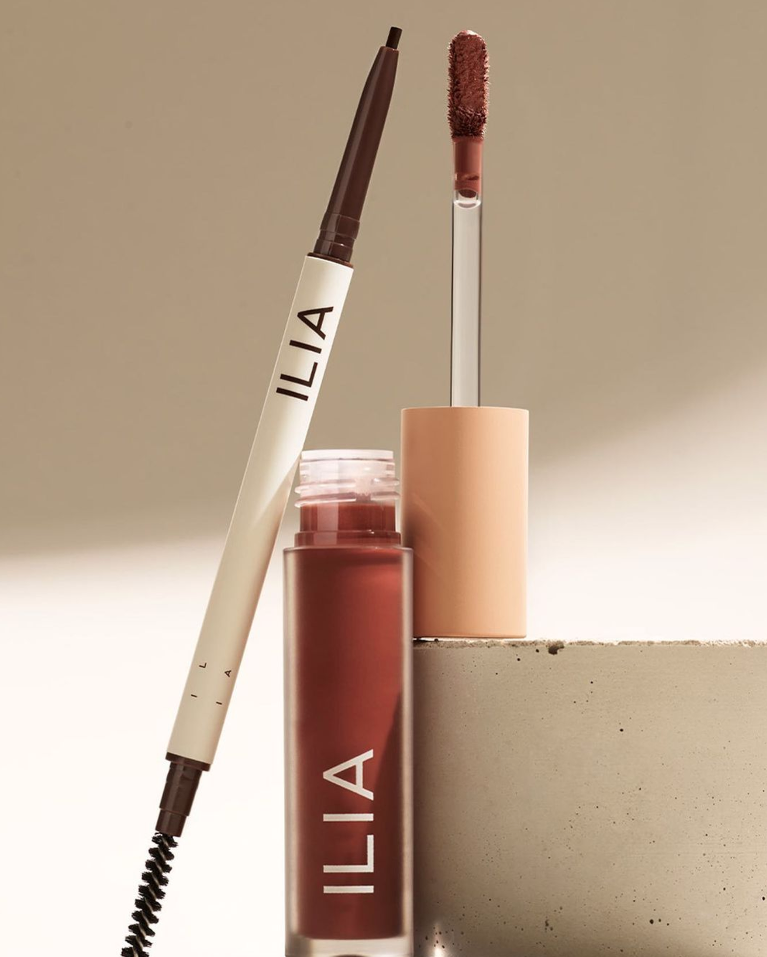 Makeup products including a liquid eyeliner, a lipstick with a sponge tip applicator, and a beige container, arranged on a neutral background.