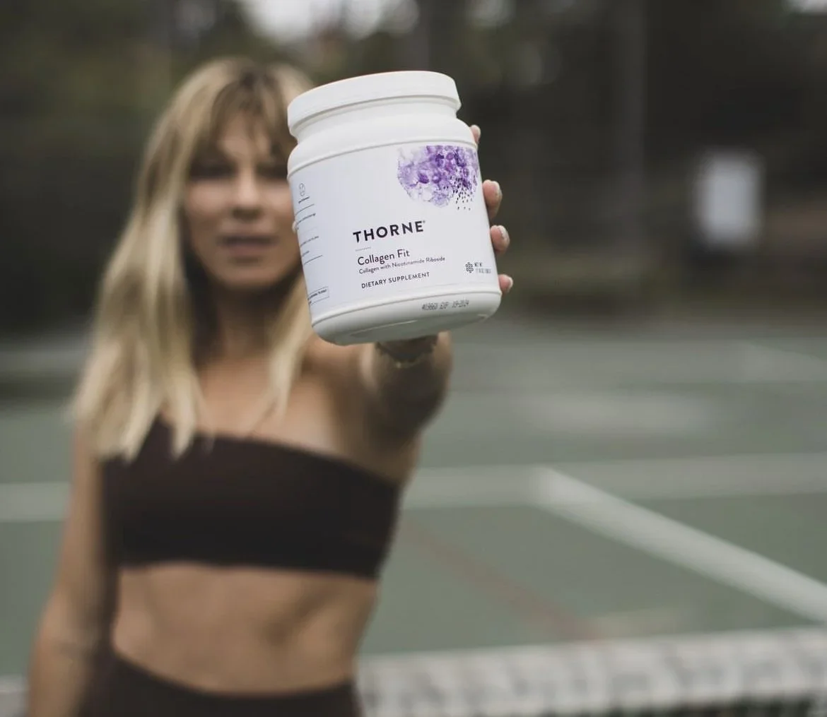 A woman holding a white container of Thorne Collagen Fit supplement towards the camera on a tennis court.