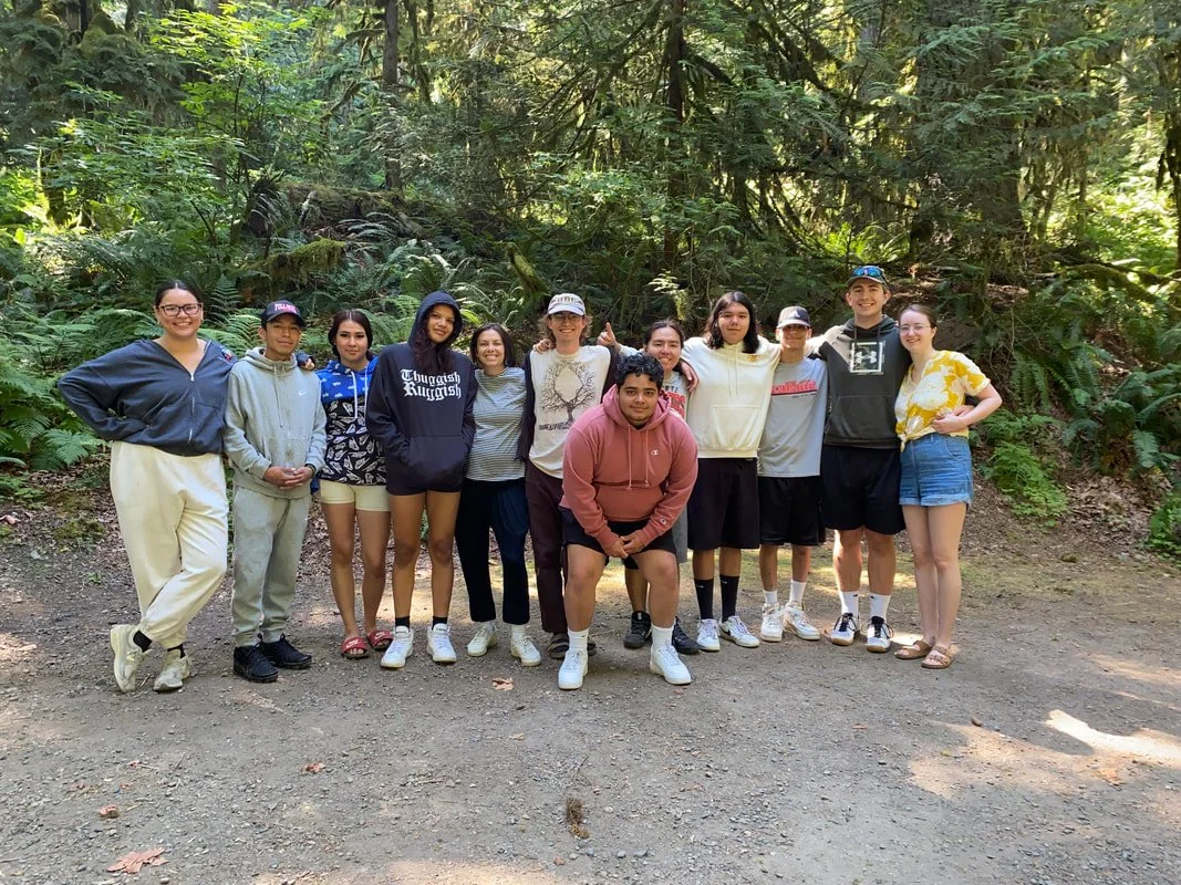 Group of 12 people standing outdoors on a trail in a forest, posing for a photo.