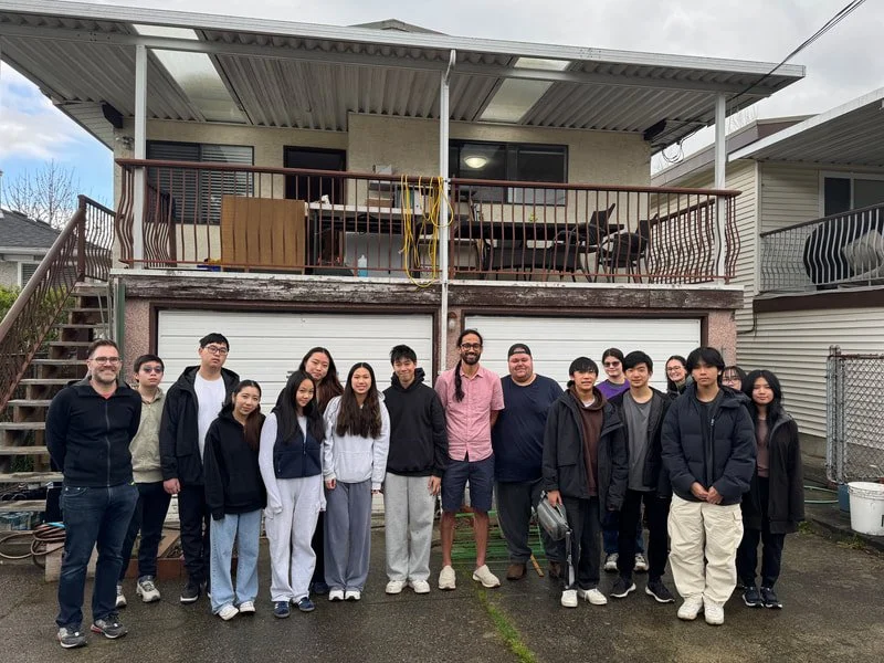 Group of 14 people standing in front of a house with a second-story balcony.