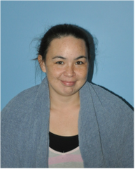 A woman with dark hair tied back, smiling, wearing a gray scarf and a layered top, seated against a blue background.