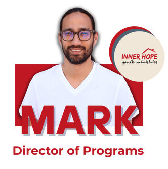 A man with glasses, a beard, and long hair in a ponytail, wearing a white shirt, standing in front of a black background with a logo that says "Inner Hope Youth Ministries."