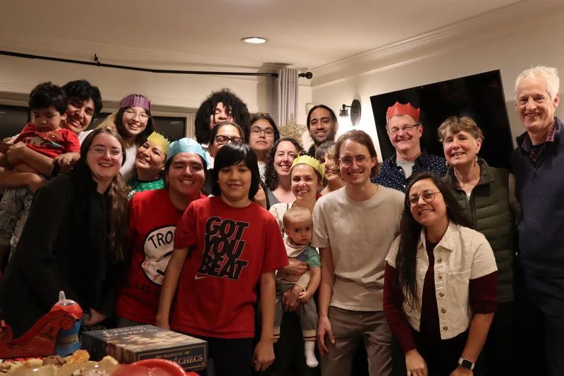 Family and friends gathered for a celebration, wearing colorful party hats and smiling.