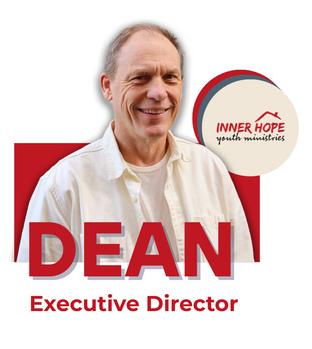 A smiling man dressed in a light-colored shirt standing in front of a logo for Inner Hope Youth Ministries, with the title Dean and the subtitle Executive Director.