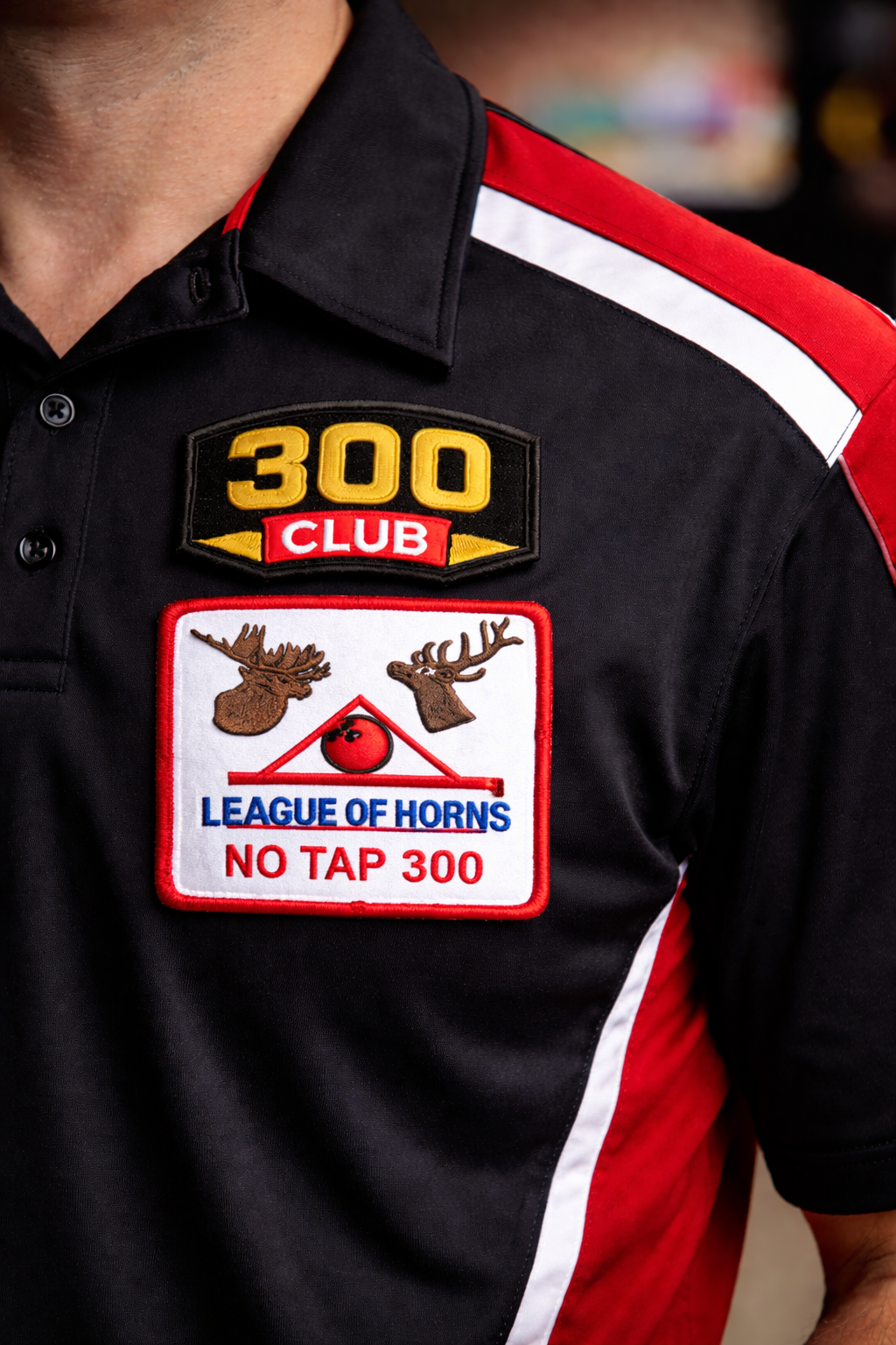 Close-up of a black and red racing shirt with patches, including one with a moose and horn design, and text related to a racing club.
