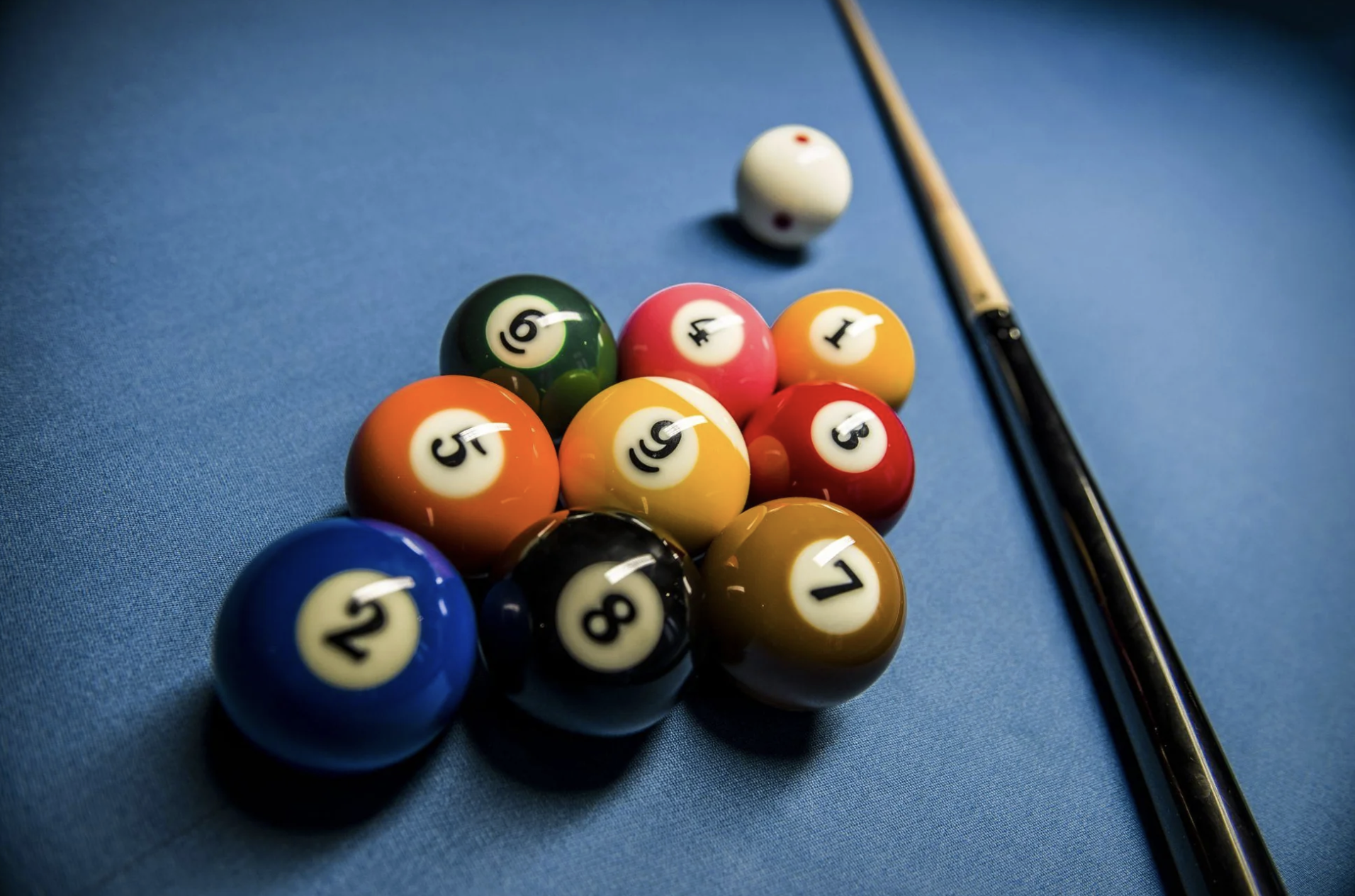 Colored billiard balls arranged in a triangle on a blue pool table near a cue stick.