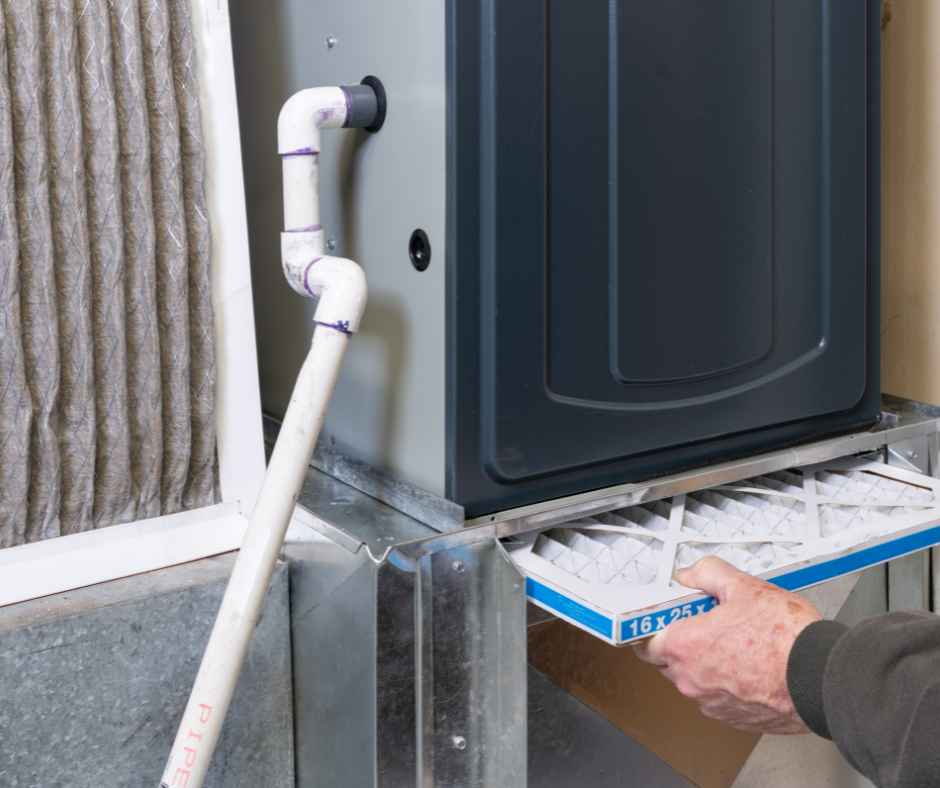 A person installing or maintaining an outdoor air conditioning unit or heat pump, with a pipe connecting to it and a cardboard box underneath.