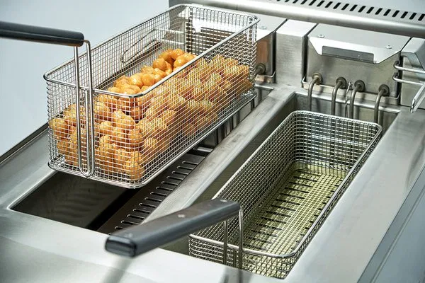 Commercial deep fryer with baskets of cooked chicken wings and empty basket for frying.