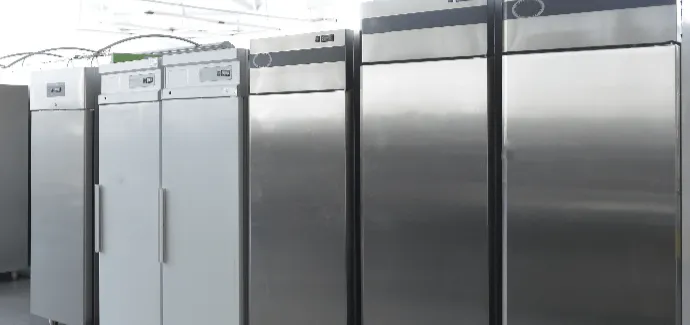Several stainless steel commercial refrigerators or freezers in a row in a kitchen or industrial setting.