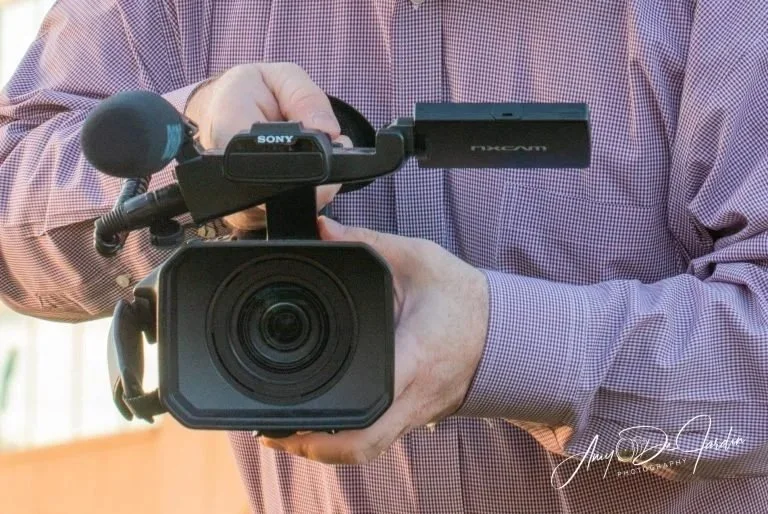 Person holding a professional video camera with a microphone attached.