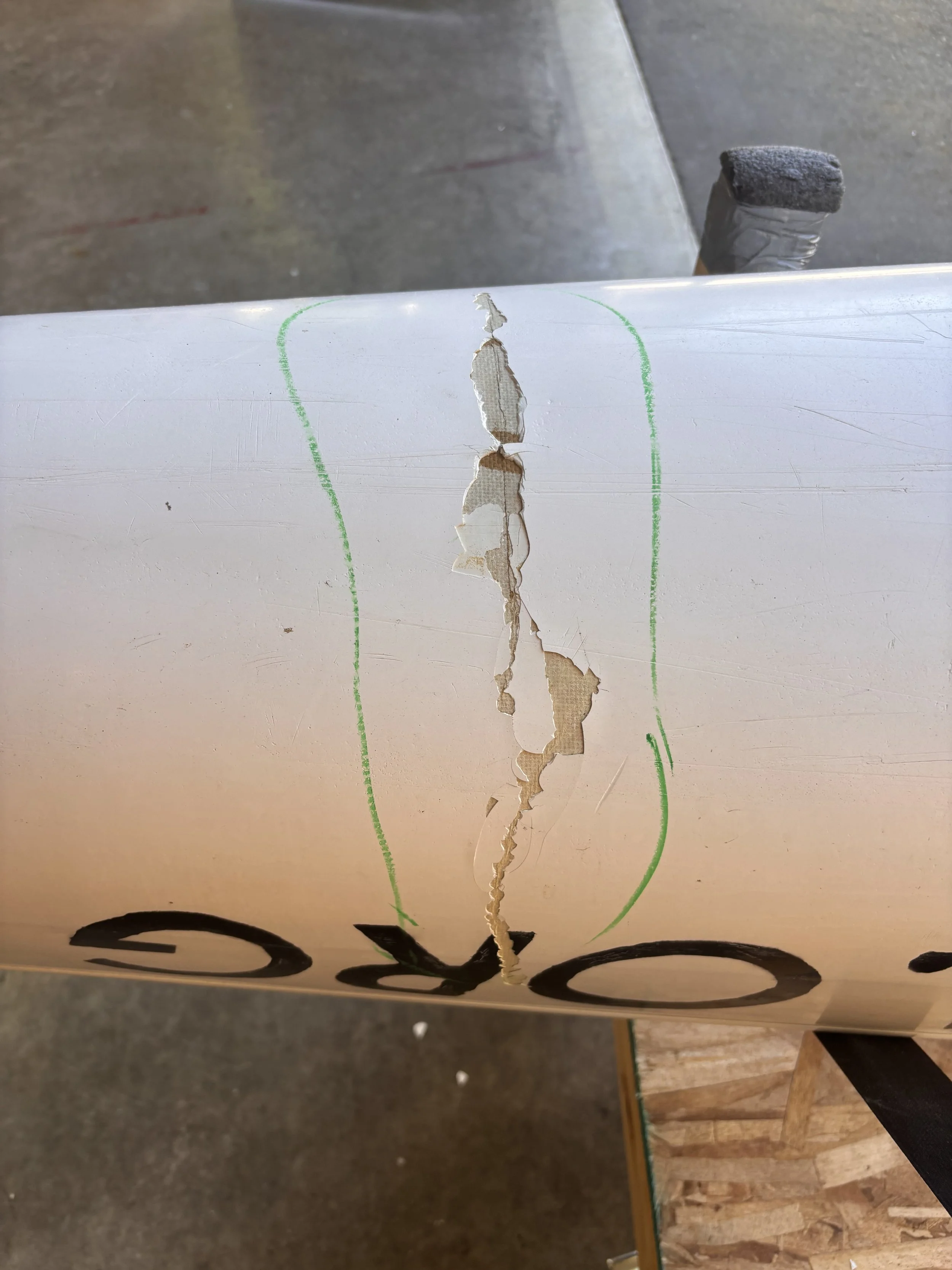 A torn piece of paper with a green outline and black lettering, torn down the middle, attached to a surface with a black table underneath. The background shows a concrete floor and wooden section.