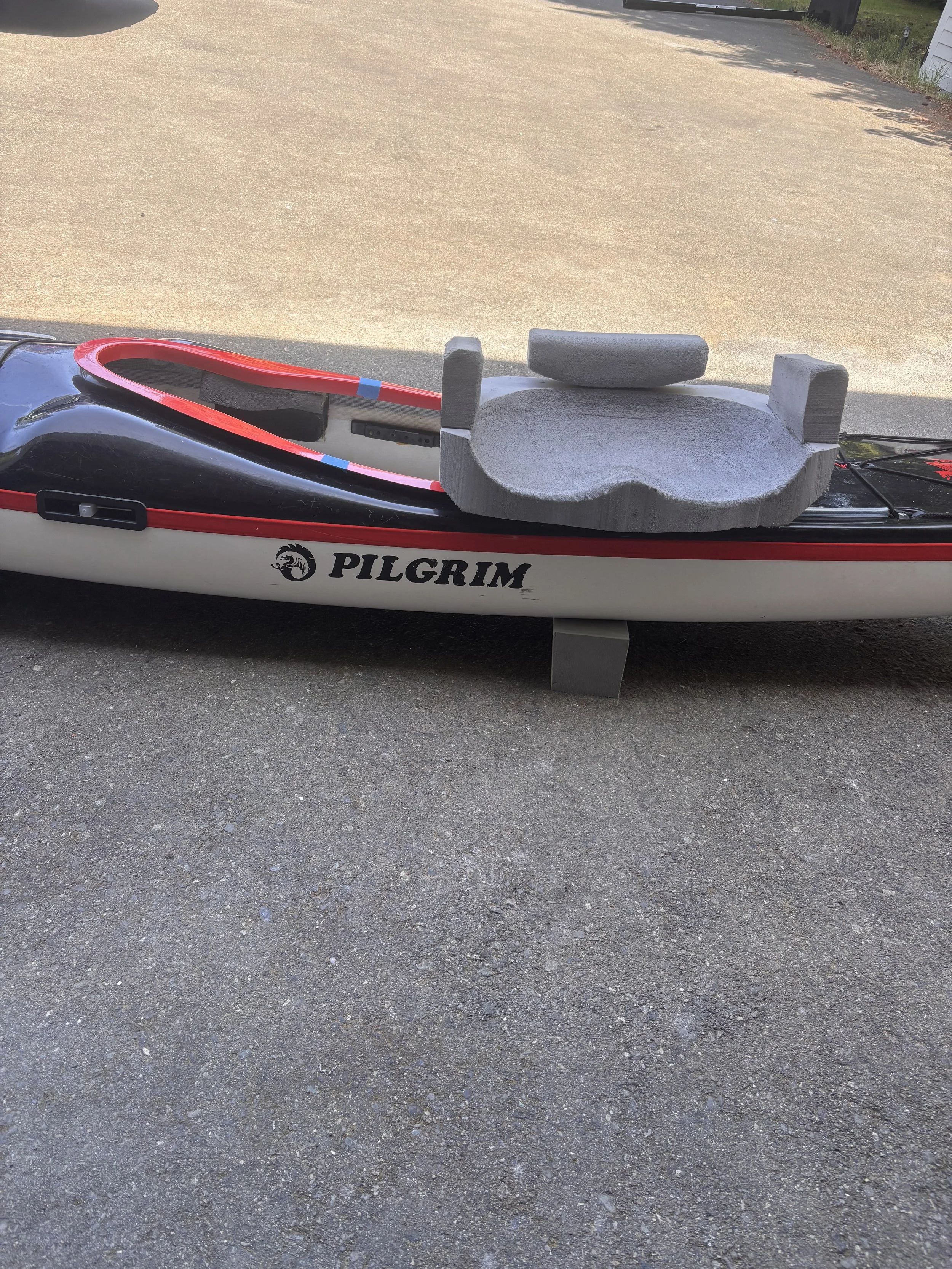 A kayak with a seat and footrests, resting on a paved surface outdoors.