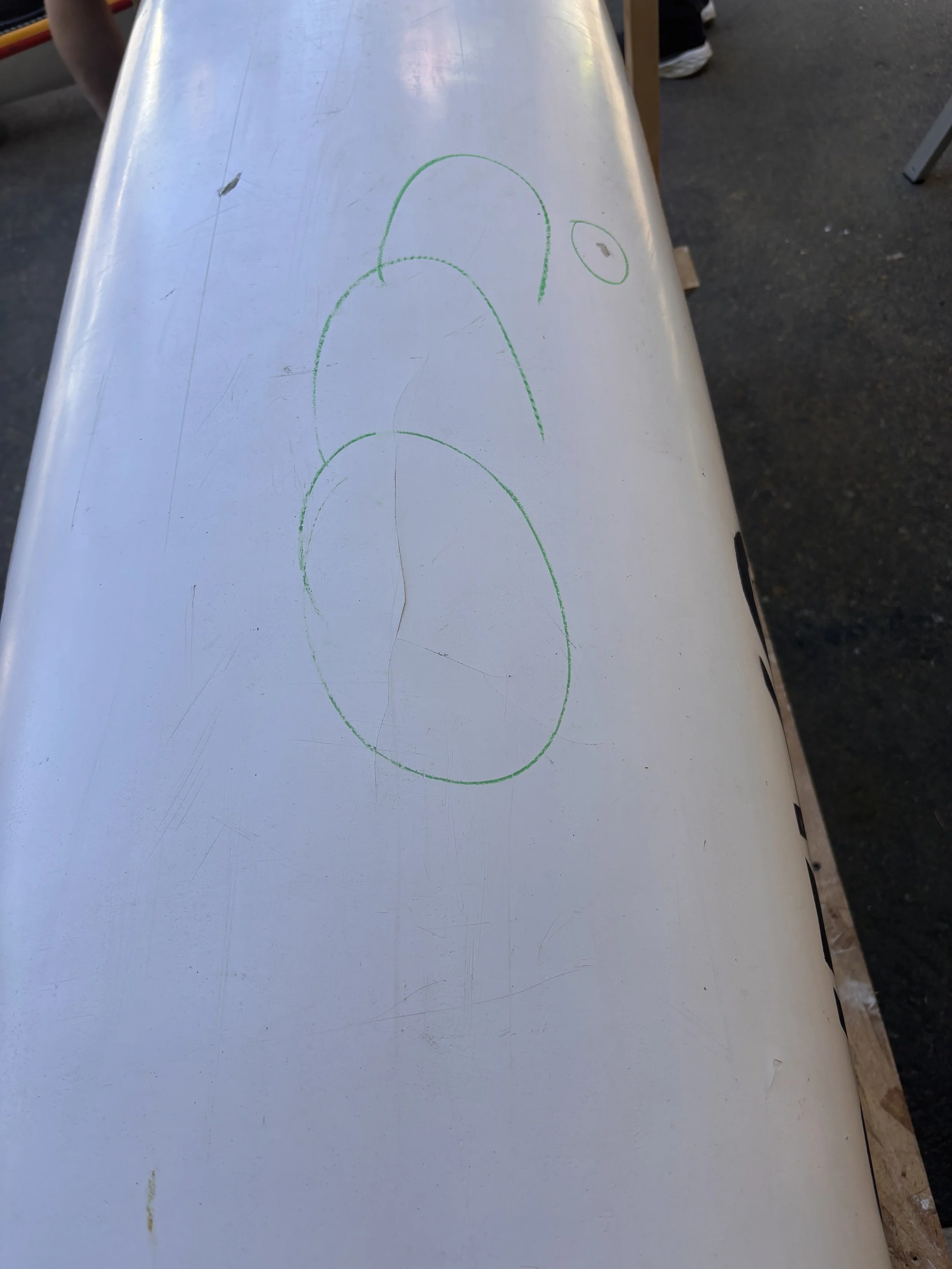 A white tabletop with green marker drawings of circles, some overlapping, on a surface with scratches and marks.