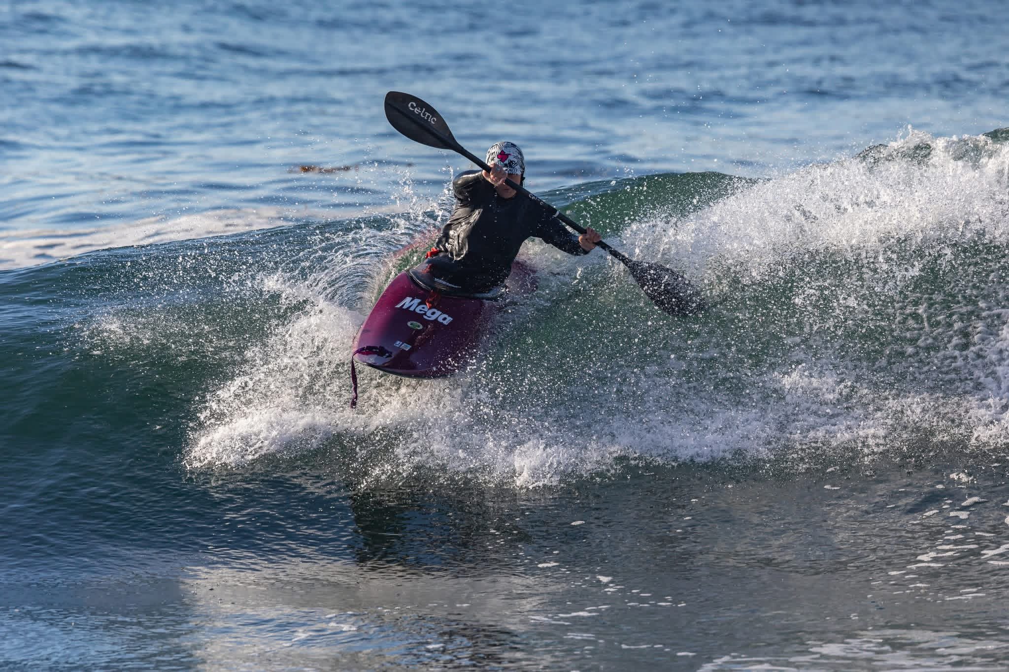 Person wearing a helmet and a black jacket surfing on a wave with a purple surfboard.