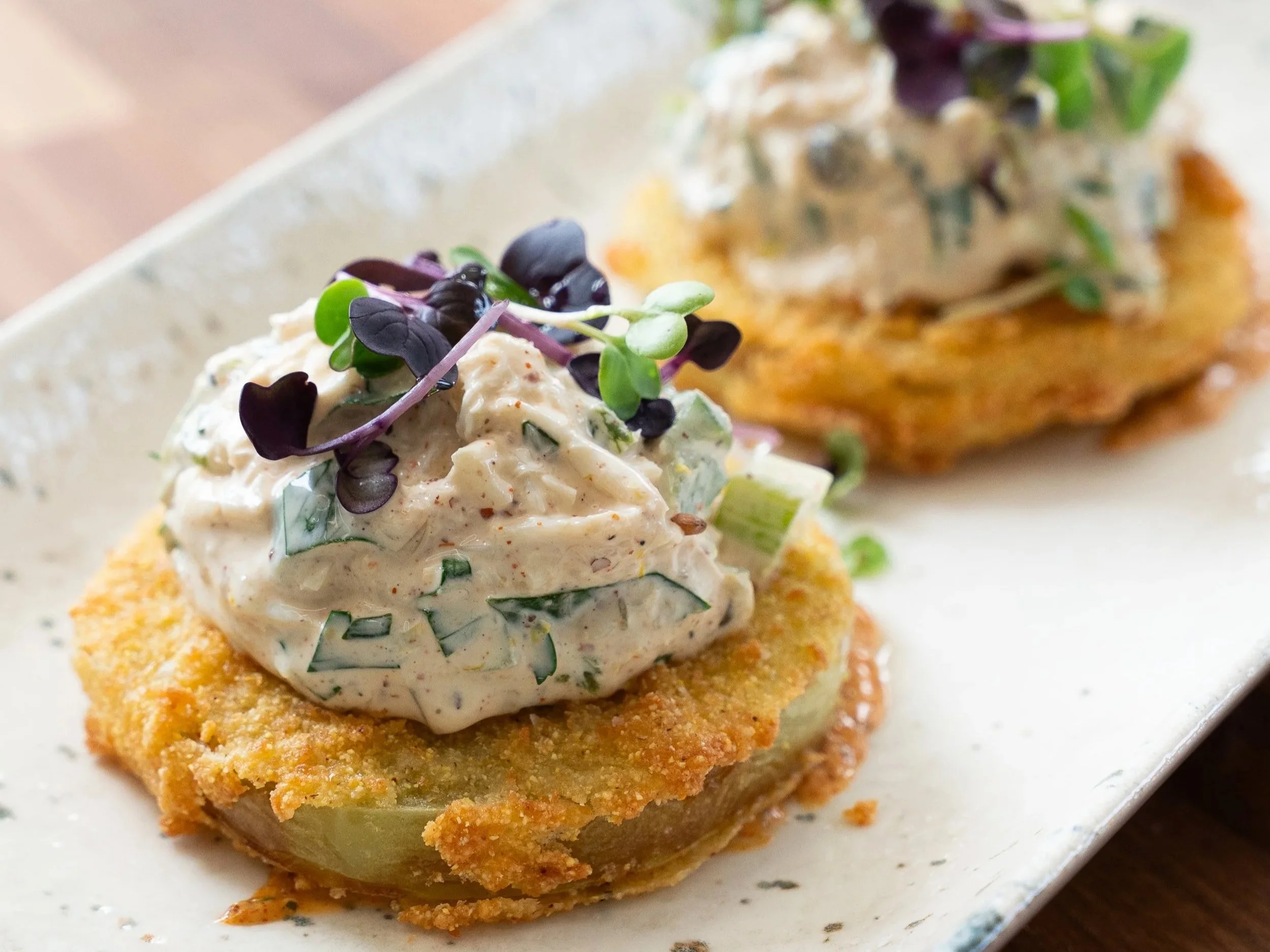 Mini square of breaded and fried food topped with creamy seafood salad garnished with microgreens.