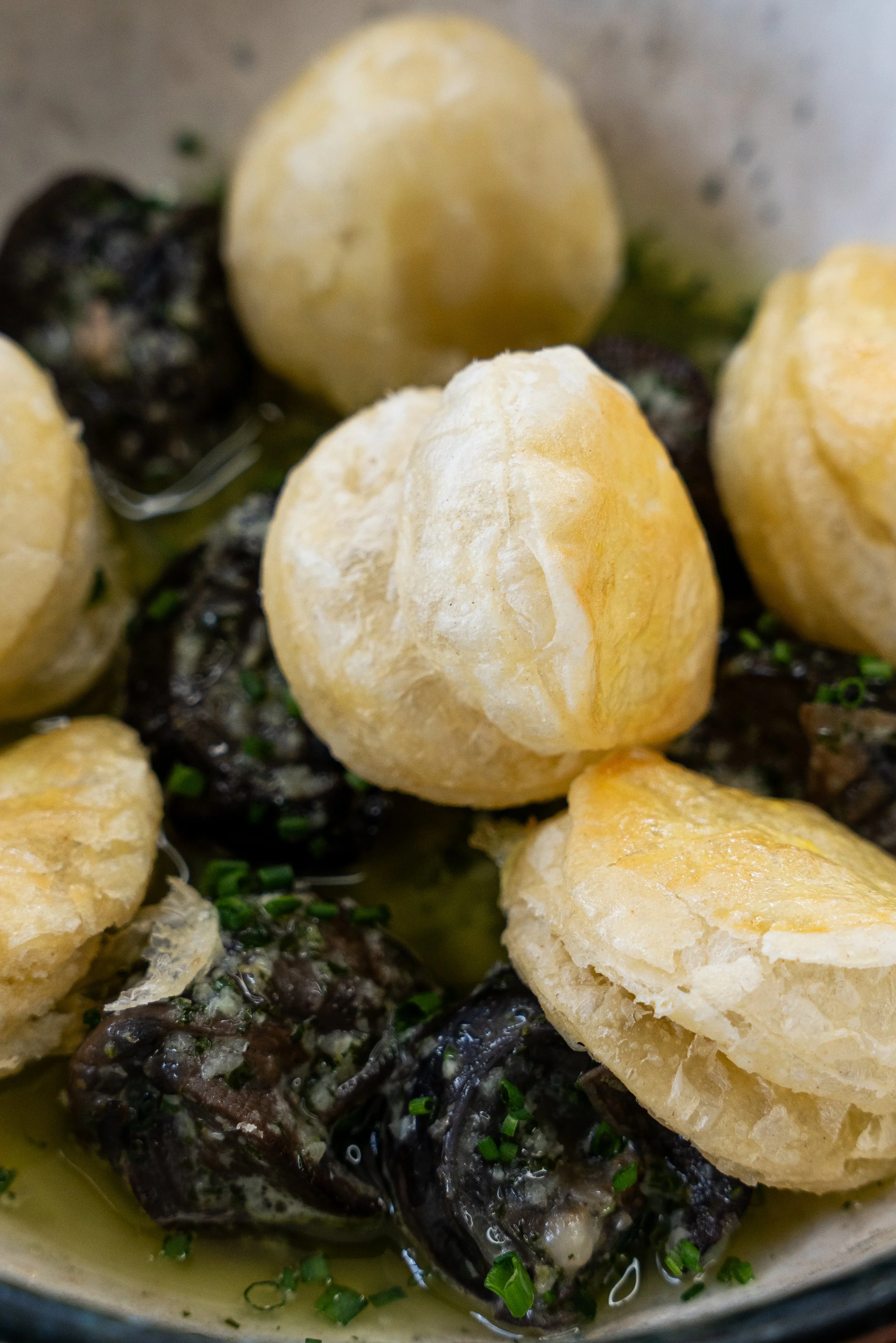 Close-up of cooked fish topped with roasted garlic and chopped green onions, served in a bowl with a lemon wedge.
