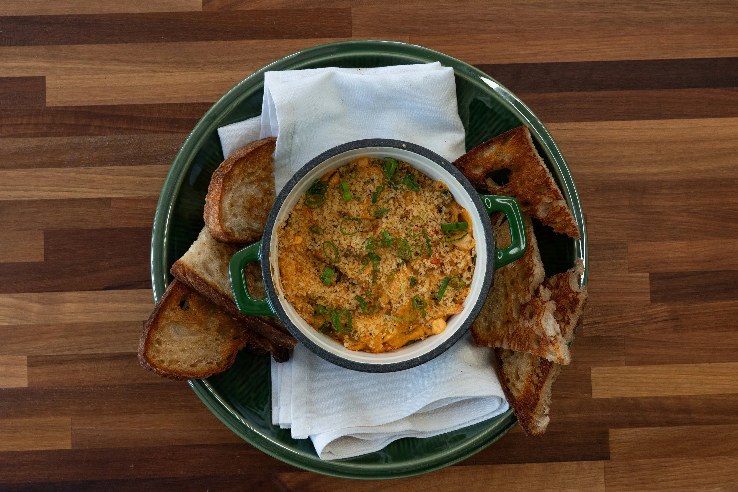 A green tray with a bowl of seasoned rice with green onions, surrounded by slices of toasted bread on a wooden table.