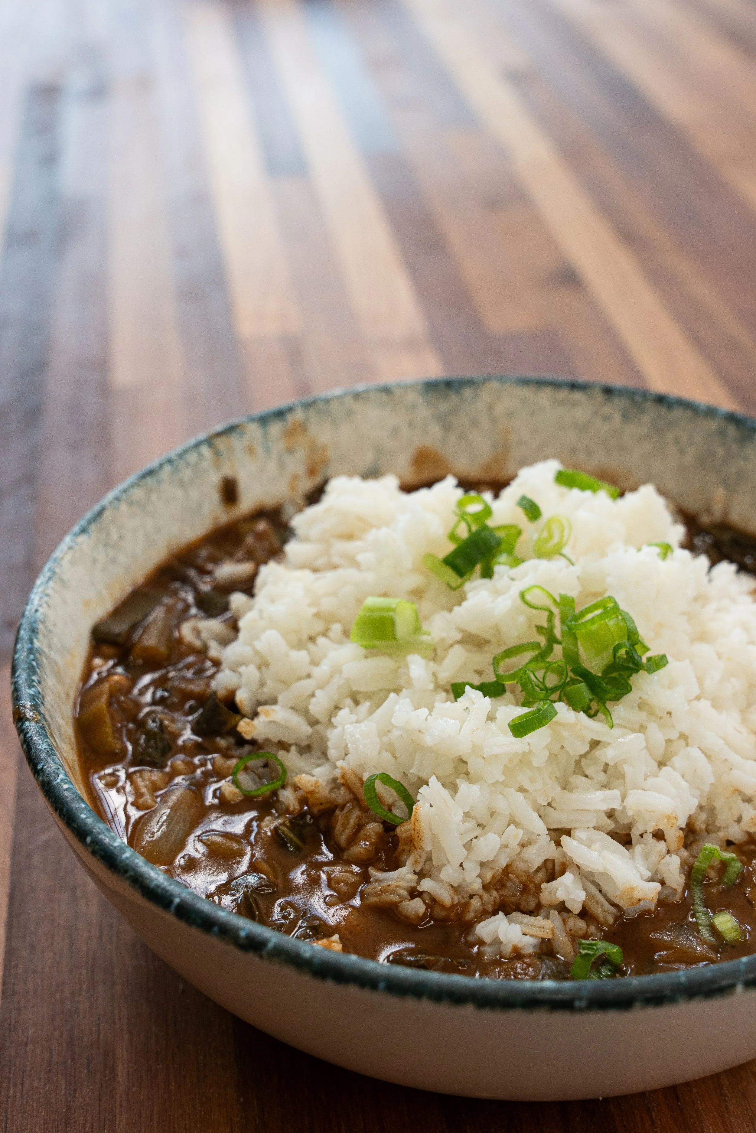 A bowl of beef stew topped with mashed potatoes and chopped green onions on a wooden table.
