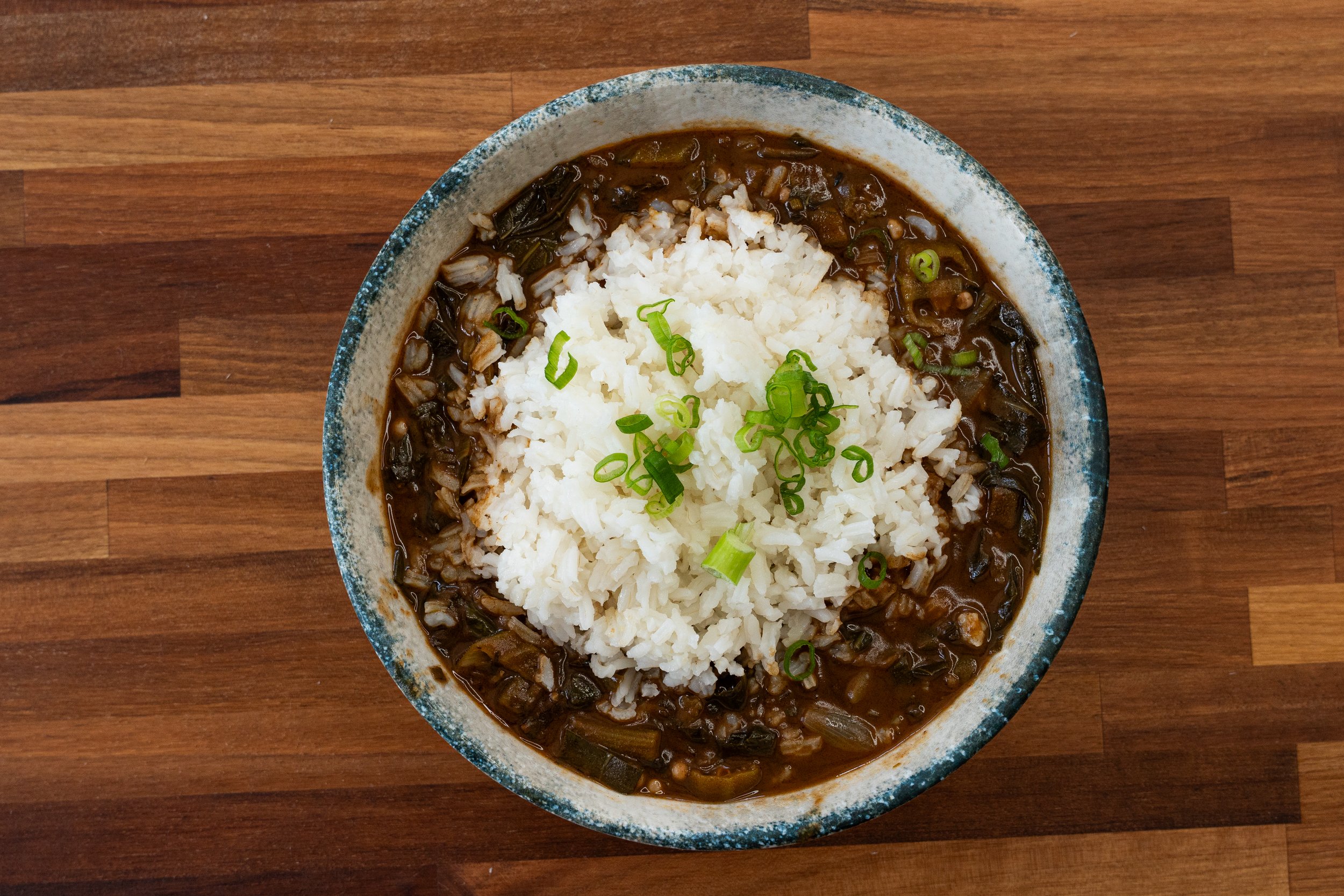 Bowl of rice and beef stew garnished with chopped green onions on a wooden surface.