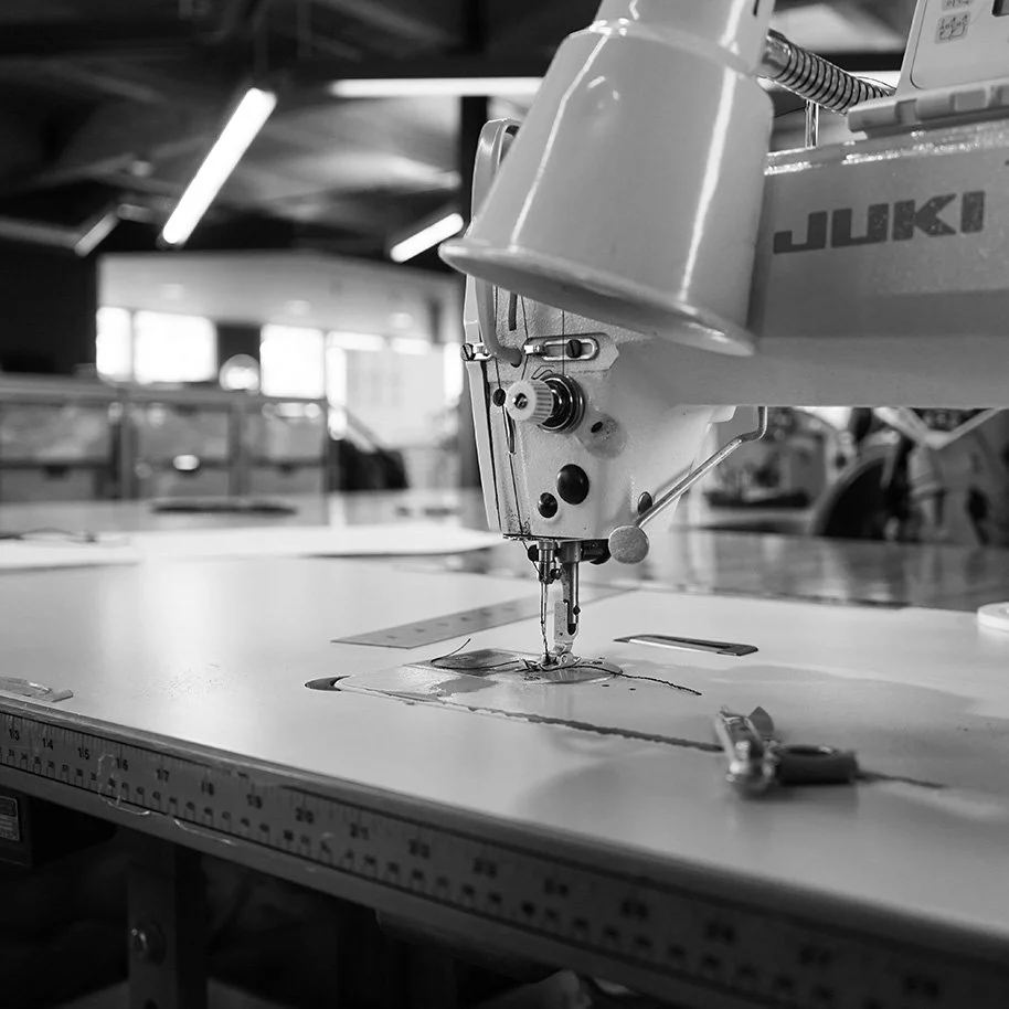 Industrial sewing machine working on fabric in workspace with tools in background