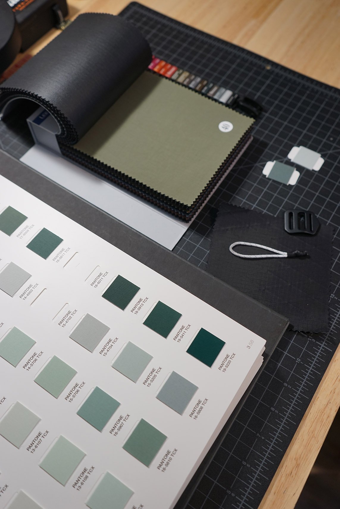 Color swatch book open on a desk next to color samples and a cutting mat.