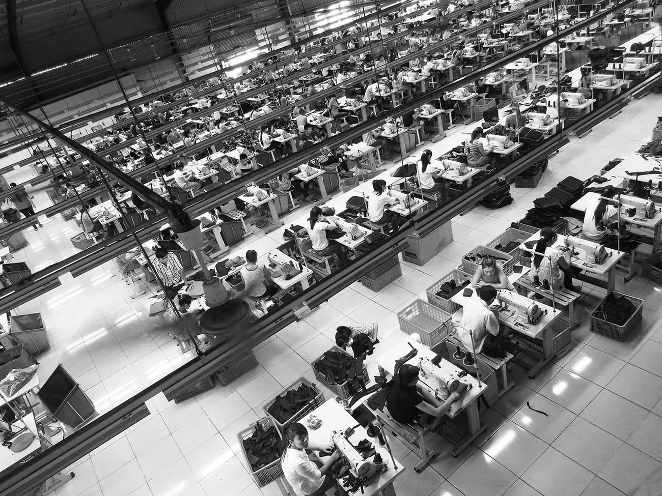 A large factory or workshop with many workers seated at sewing machines, working at their stations in an organized and well-lit environment.