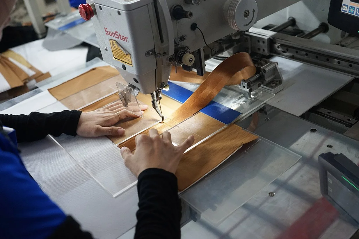 A person operating a sewing machine stitching a piece of wood veneer or thin plywood.