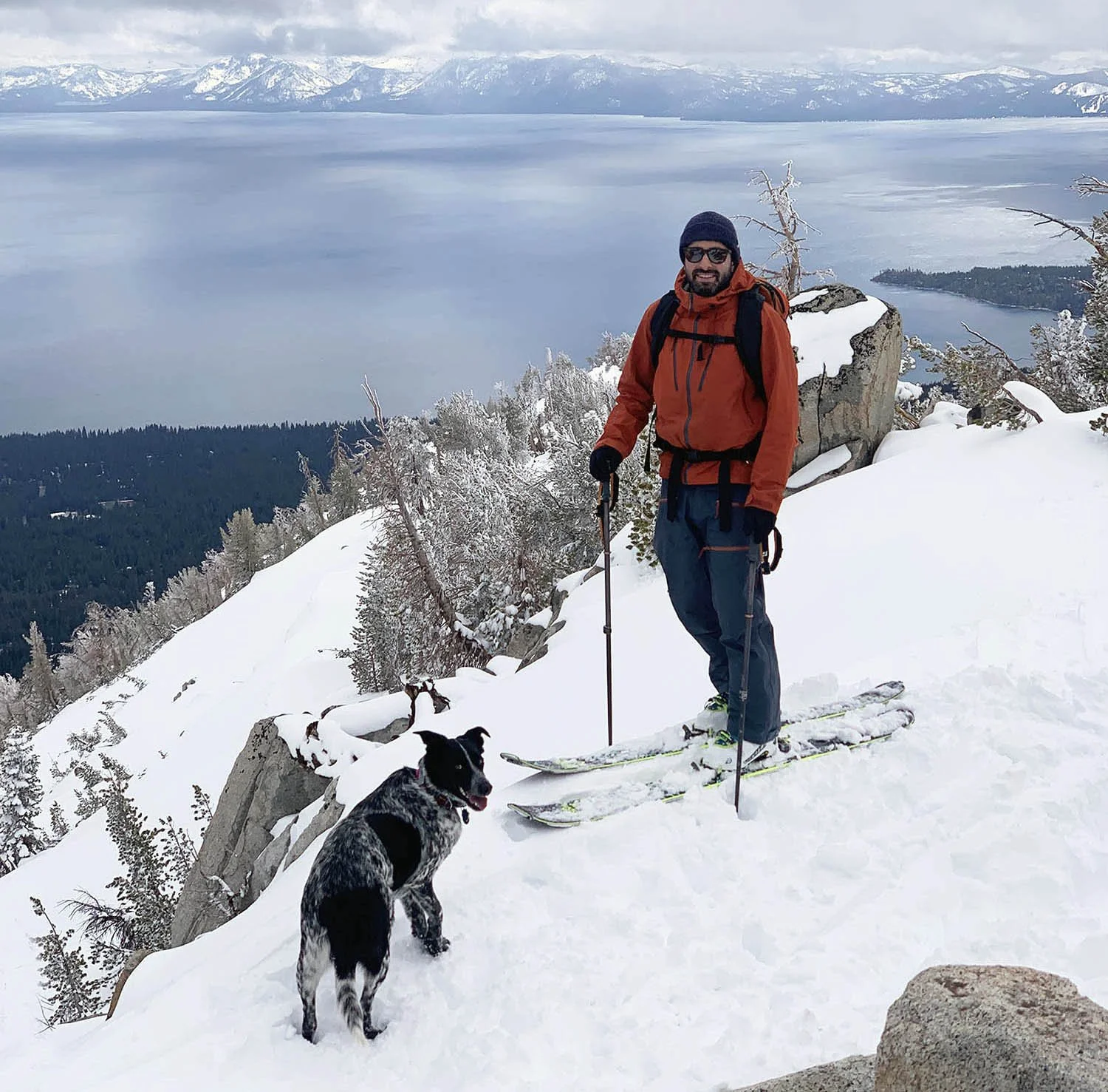 Founder, Rawmin Ehyai standing on snow-covered mountain in Lake Tahoe with dog, overlooking a lake and snow-capped mountains in the distance.