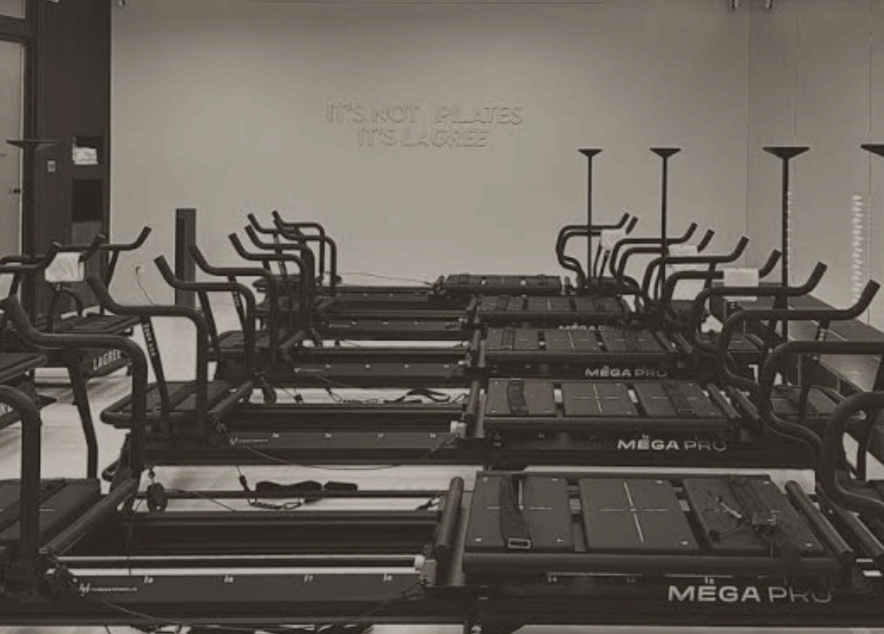 Row of reformers in a lagree studio in lewiston, id, black, facing a wall with a "It's not pilates, it's lagree" sign.