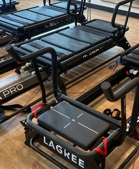 Multiple Pilates reformer machines with black canvases, metal frames, and footbars in a Lagree studio.