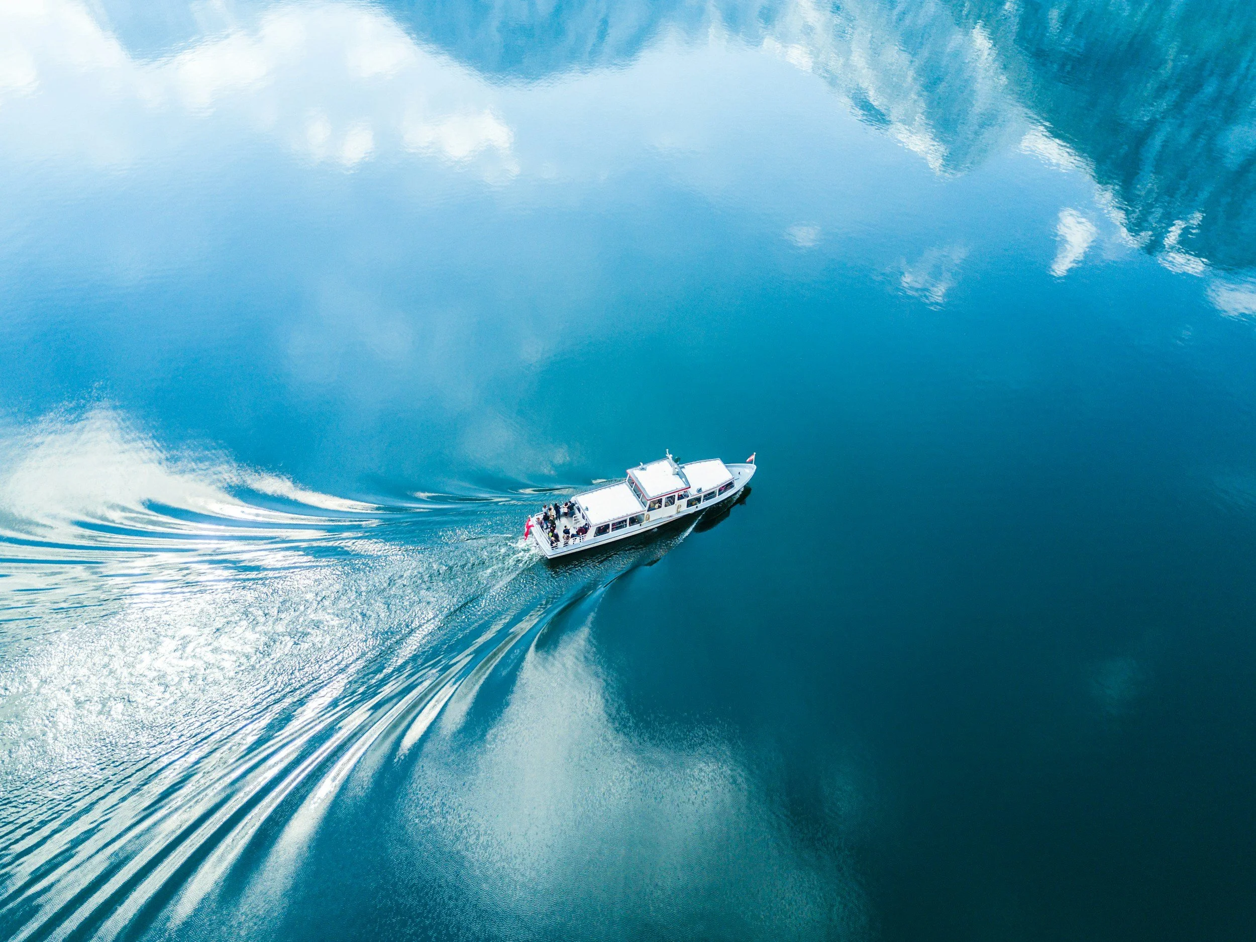 A boat sailing on a calm, reflective body of water with mountains in the background.