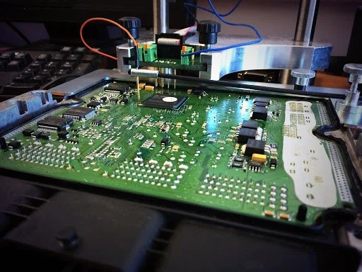Close-up of a green circuit board with various electronic components, connected to wires and metal heatsinks, on a workbench.