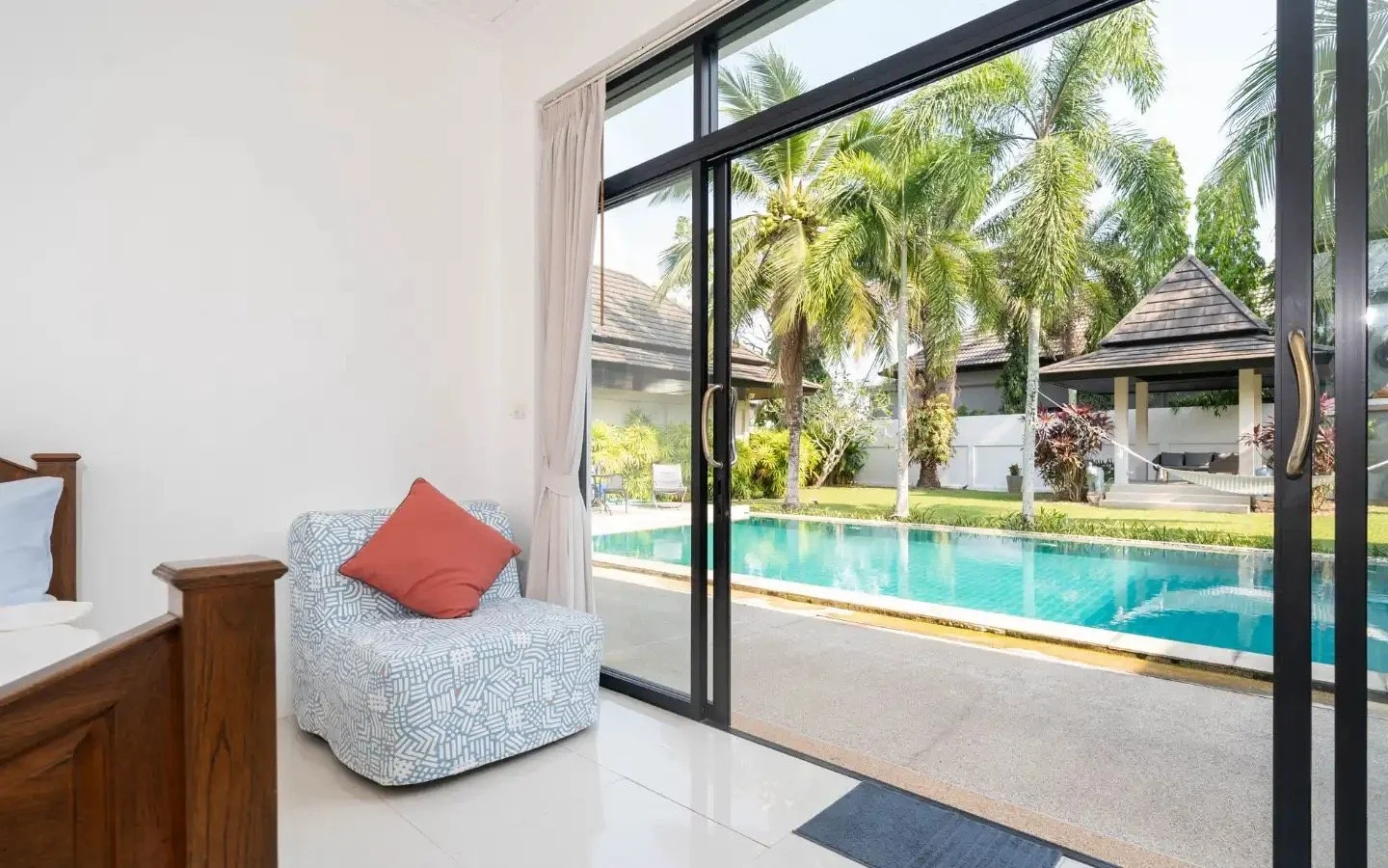Room with sliding glass door opening to a backyard with a swimming pool, palm trees, and a gazebo. Villa Lotus Heaven, Cherng Talay, Phuket