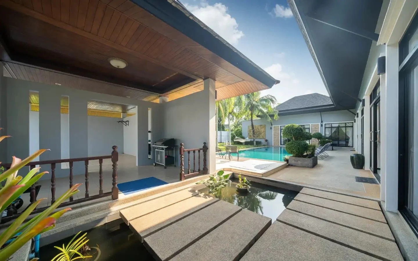A backyard with a swimming pool, lounge chairs, tropical plants, and a covered patio area. Villa Lotus Heaven, Cherng Talay, Phuket