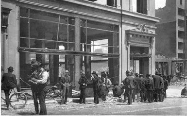 Black and white photo of people gathered outside a building, some standing in line, with a few bicycles nearby, in an urban setting.
