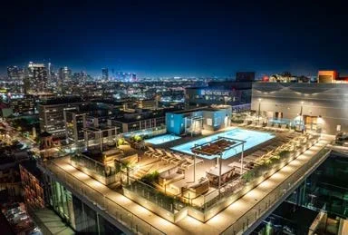 Night view of a rooftop pool area on a high-rise building with city skyline in the background, illuminated with lights.