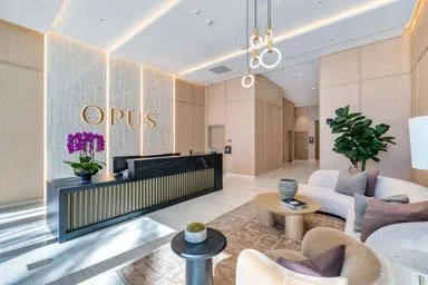 Modern lobby with reception desk, seating area with white and beige furniture, potted plant, and OPUS sign on wall.