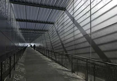 A long pedestrian walkway enclosed by metal and glass walls and ceiling, with two people walking in the distance.