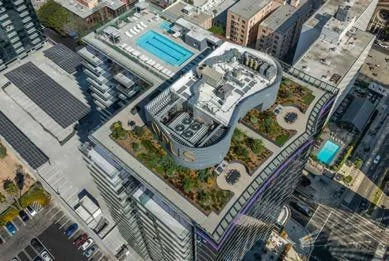 Aerial view of a modern high-rise building with a rooftop pool and gardens in an urban area.