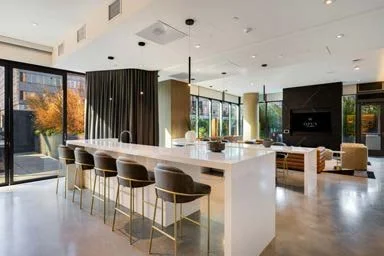 Modern open-concept living space with a kitchen island, barstools, a seating area, large windows, and a television.