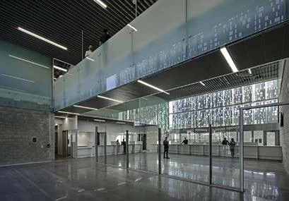 Modern airport terminal with high ceilings, large glass windows, and a digital display board. People are walking and waiting inside the spacious, well-lit area.