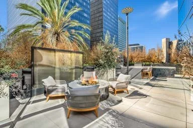 Outdoor patio area with round table and four chairs, overlooking a cityscape with tall buildings and palm trees on a sunny day.